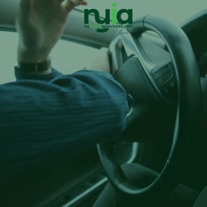 Person in a car pressing the horn on the steering wheel, seen from the passenger side.