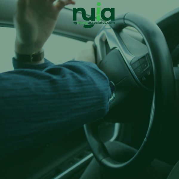 Person in a car pressing the horn on the steering wheel, seen from the passenger side.