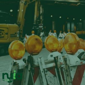 Four yellow construction warning lights are mounted on barricades at a worksite in Northampton, with No Fault Insurance Doctors and construction equipment visible in the background.