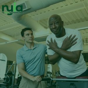 A physical therapist assists an older man performing an exercise on a treadmill in a gym, similar to the rehabilitation support offered by no-fault insurance doctors in Franklin Square.