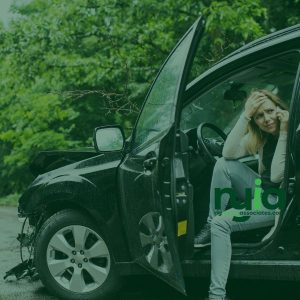 A woman sits in the driver's seat of a car with a damaged front end and an open door, holding her head in distress—she may need an auto accident doctor in Amityville.